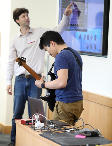 A student demonstrates vibrations using an electric guitar. The readings are projected on a screen in the classroom.